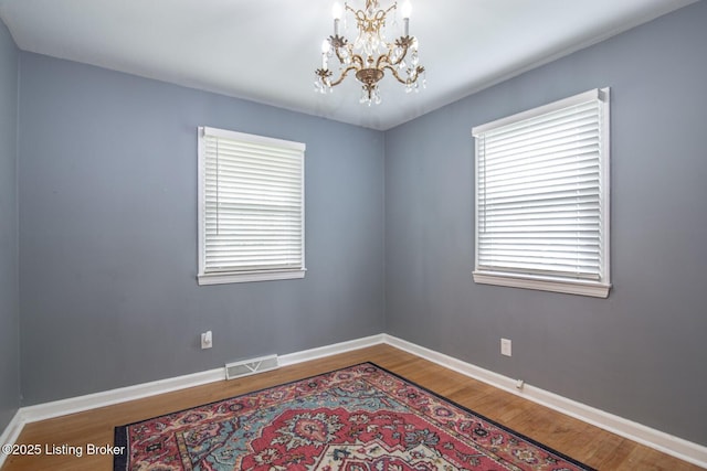 empty room featuring visible vents, baseboards, a notable chandelier, and wood finished floors