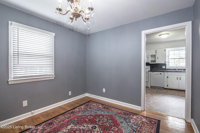 empty room with a chandelier, wood finished floors, a sink, and baseboards