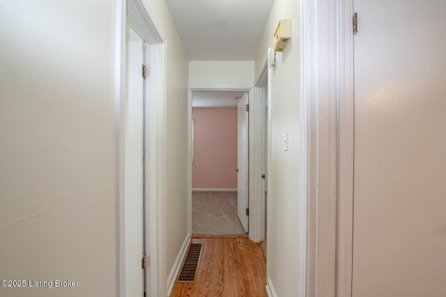hallway with light wood finished floors, baseboards, and visible vents