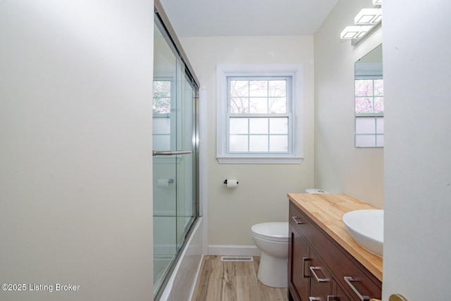 bathroom featuring baseboards, toilet, enclosed tub / shower combo, vanity, and wood finished floors