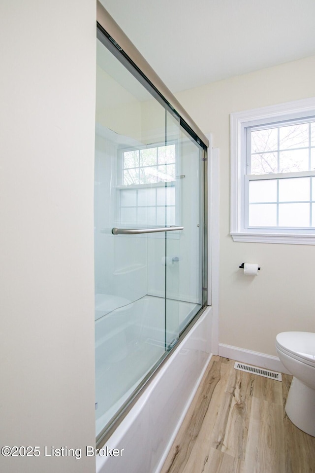bathroom with combined bath / shower with glass door, baseboards, toilet, visible vents, and wood finished floors