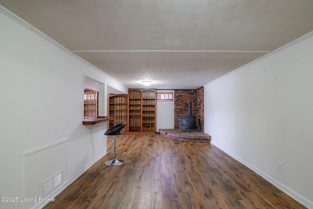 unfurnished living room featuring crown molding, wood finished floors, a wood stove, and visible vents