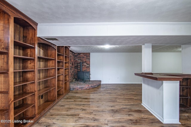 basement with visible vents, a wood stove, wood finished floors, and baseboards