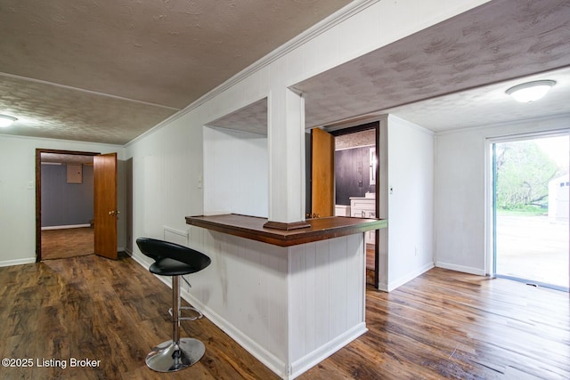 bar featuring a textured ceiling, baseboards, ornamental molding, and wood finished floors