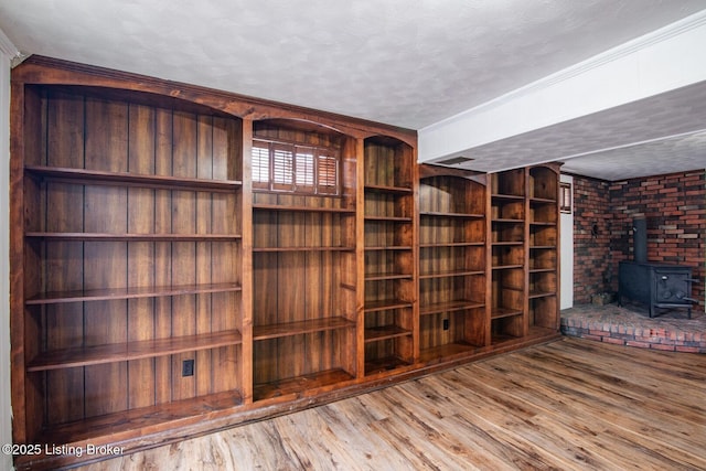 unfurnished living room with a textured ceiling, wood finished floors, a wood stove, and ornamental molding