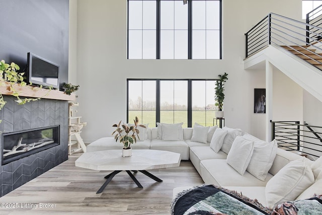 living area featuring a tiled fireplace, wood finished floors, a high ceiling, and a wealth of natural light