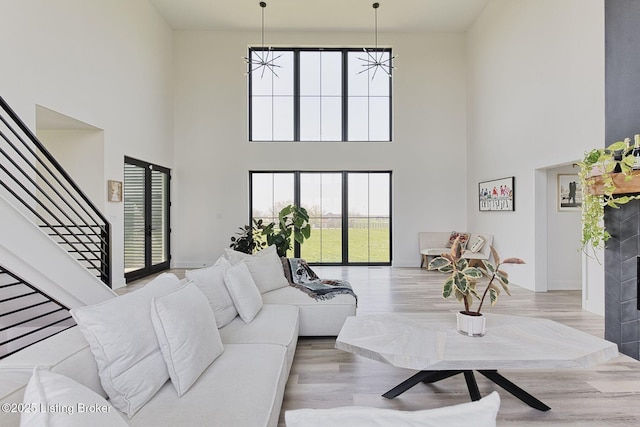 living room featuring stairway, baseboards, a high ceiling, and light wood-style flooring