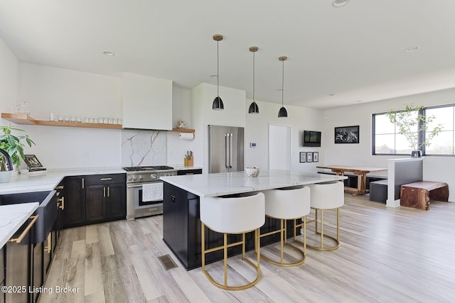 kitchen featuring light wood-type flooring, a kitchen bar, open shelves, light stone countertops, and high quality appliances