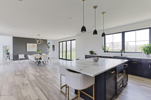 kitchen with dark cabinets, a sink, stainless steel microwave, a center island, and light wood-style flooring