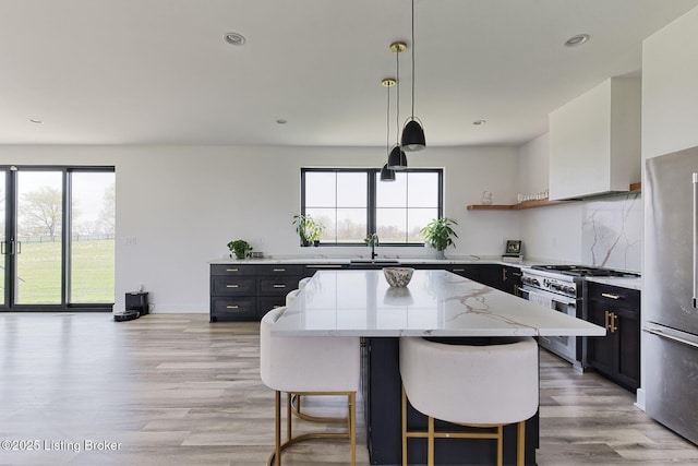 kitchen with dark cabinets, a kitchen island, light stone countertops, wall chimney exhaust hood, and appliances with stainless steel finishes