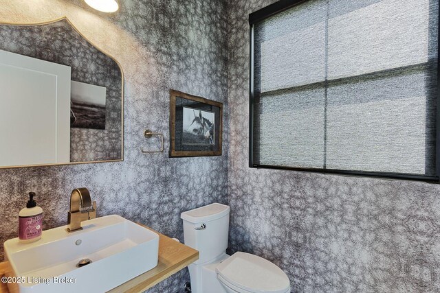 half bathroom with wallpapered walls, a sink, and toilet
