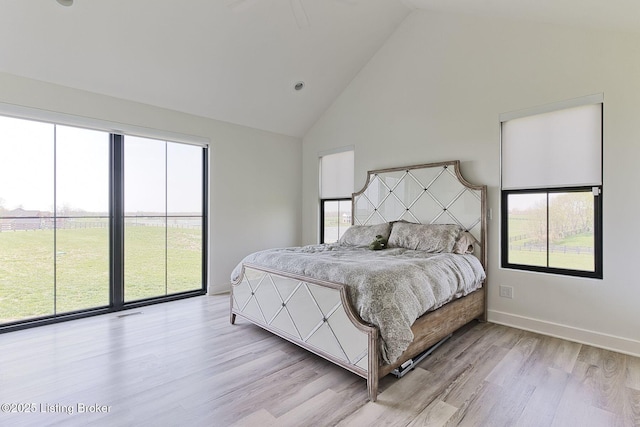 bedroom featuring baseboards, high vaulted ceiling, light wood-style floors, and multiple windows