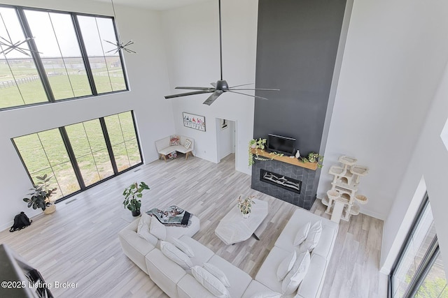 living area with baseboards, a ceiling fan, wood finished floors, a high ceiling, and a fireplace