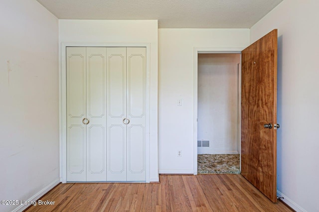unfurnished bedroom with wood finished floors, a closet, visible vents, and baseboards