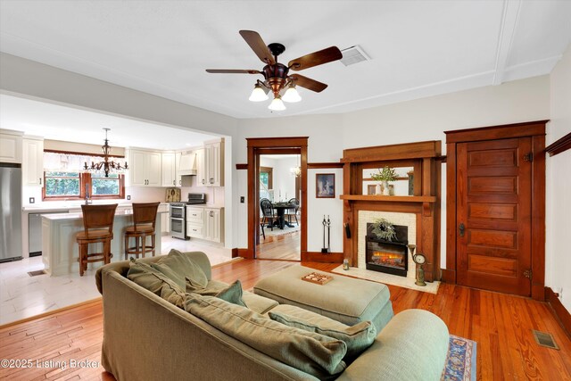 205 Birch Ave, La Grange, KY 40031 - living room featuring light wood-type flooring, visible vents, ceiling fan with notable chandelier, and a fireplace with flush hearth