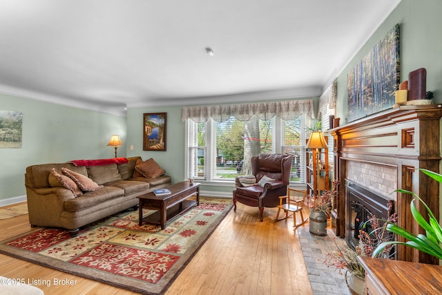 living room featuring wood-type flooring, a fireplace, baseboards, and ornamental molding
