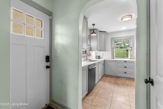 kitchen featuring a sink, dishwasher, arched walkways, light countertops, and backsplash