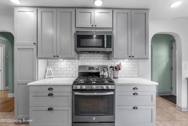 kitchen with light countertops, arched walkways, appliances with stainless steel finishes, and gray cabinets