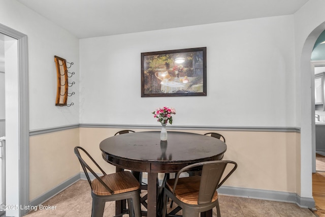 tiled dining area featuring baseboards and arched walkways