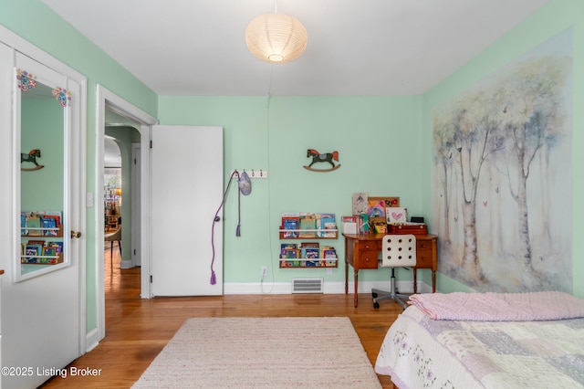 bedroom with arched walkways, wood finished floors, visible vents, and baseboards