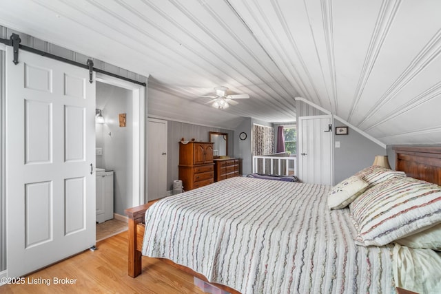 bedroom with a barn door, vaulted ceiling, and wood finished floors
