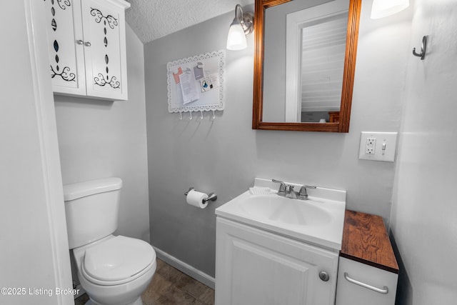 bathroom with toilet, vanity, a textured ceiling, and baseboards