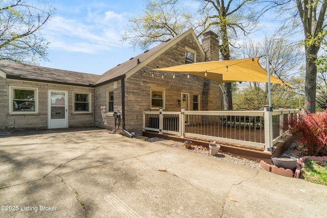 back of property featuring stone siding, a patio area, a chimney, and a deck