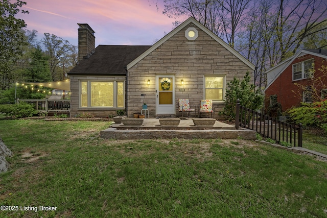 rear view of property with stone siding, a chimney, fence, and a yard