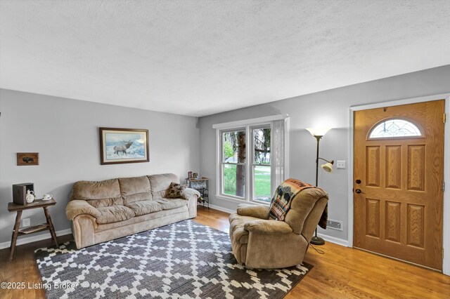 living area featuring a textured ceiling, wood finished floors, and baseboards