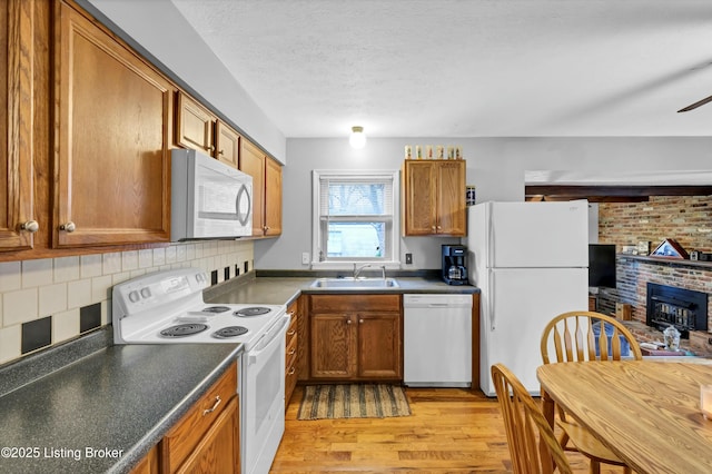 kitchen with white appliances, brown cabinetry, a sink, dark countertops, and light wood finished floors