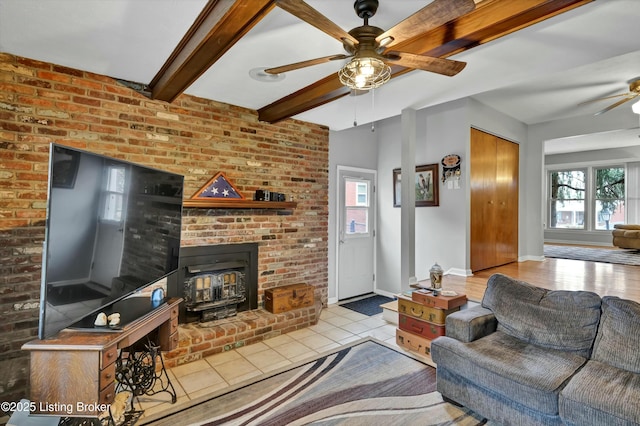 tiled living area featuring a wood stove, plenty of natural light, a ceiling fan, and beam ceiling