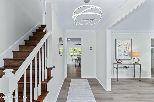 foyer entrance with wood finished floors, crown molding, baseboards, stairs, and a notable chandelier