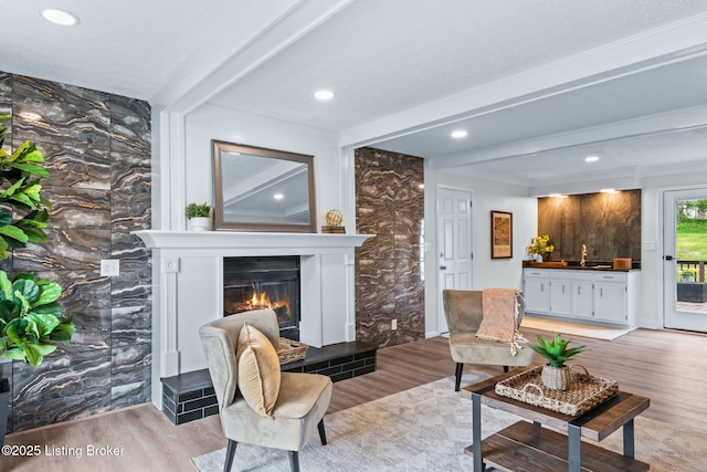 sitting room featuring recessed lighting, a glass covered fireplace, light wood-type flooring, and beam ceiling