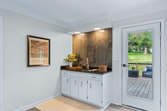 bar featuring light wood finished floors, baseboards, a sink, and ornamental molding