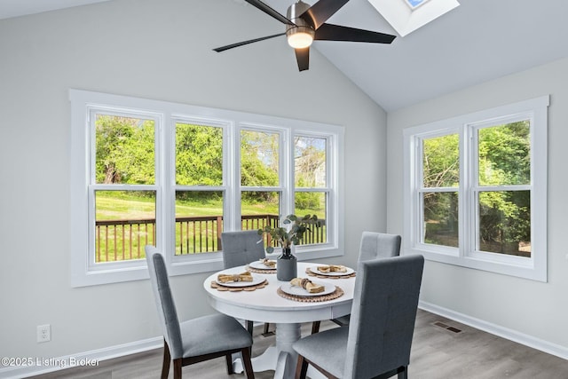 dining area with a ceiling fan, wood finished floors, lofted ceiling with skylight, baseboards, and visible vents