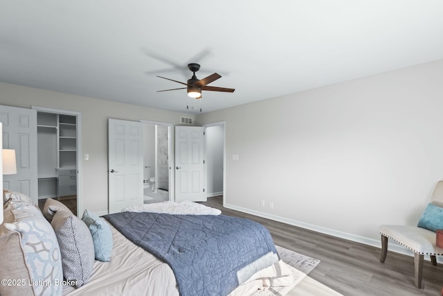 bedroom featuring wood finished floors, visible vents, a ceiling fan, a walk in closet, and baseboards