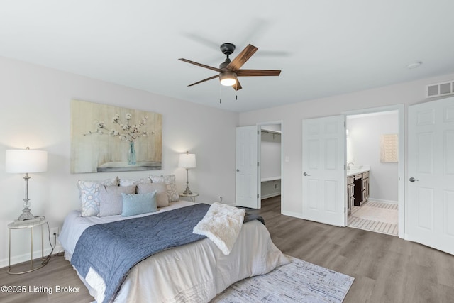 bedroom with wood finished floors, a spacious closet, baseboards, ensuite bath, and visible vents