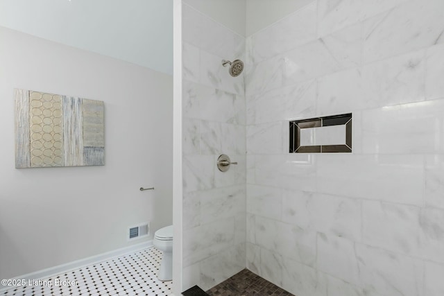 bathroom with a tile shower, toilet, visible vents, and baseboards