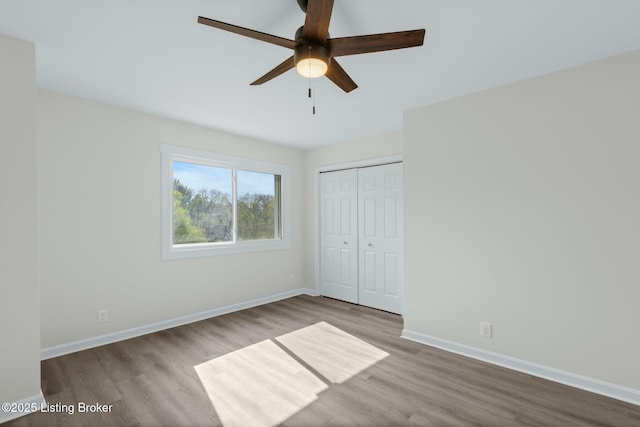unfurnished bedroom with baseboards, a ceiling fan, wood finished floors, and a closet