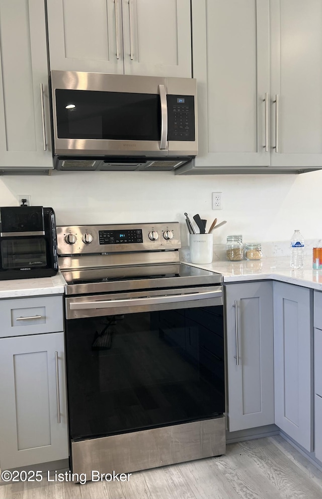 kitchen with light wood-style floors, appliances with stainless steel finishes, a toaster, and gray cabinetry