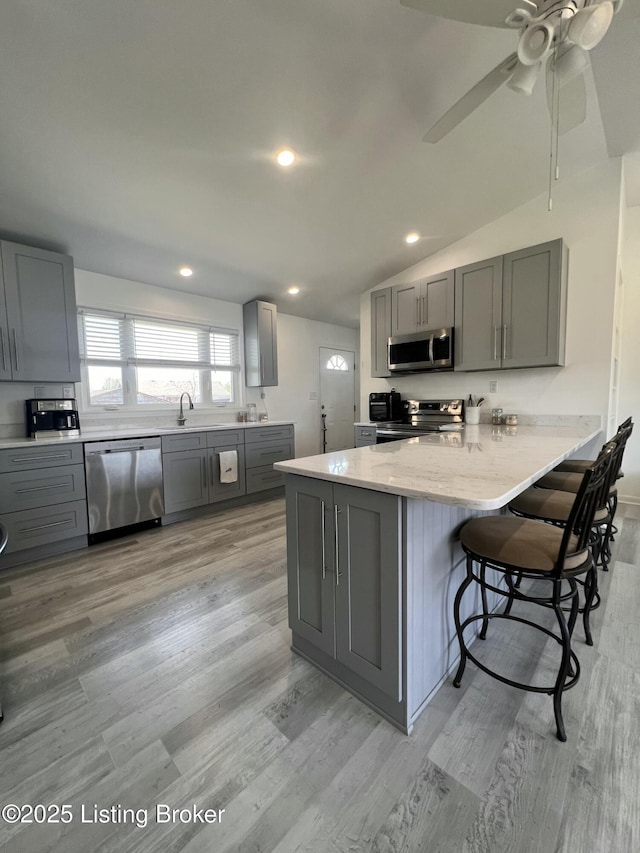 kitchen featuring a breakfast bar, gray cabinetry, light wood-style floors, and appliances with stainless steel finishes