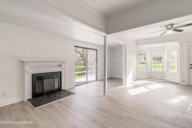 unfurnished living room with plenty of natural light, a ceiling fan, wood finished floors, and a glass covered fireplace
