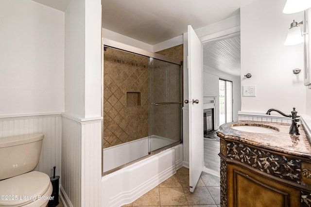 full bathroom with tile patterned flooring, enclosed tub / shower combo, toilet, vanity, and wainscoting