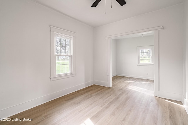 spare room featuring light wood-style floors, a wealth of natural light, baseboards, and ceiling fan