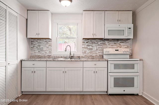 kitchen with a sink, white appliances, light wood-type flooring, tasteful backsplash, and a textured ceiling