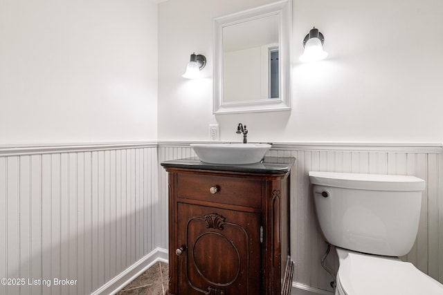 half bathroom with vanity, toilet, and a wainscoted wall
