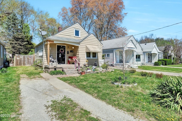 bungalow-style house featuring covered porch, a chimney, a front lawn, and fence