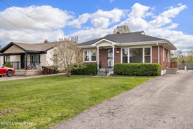 bungalow featuring roof with shingles, a front yard, and brick siding