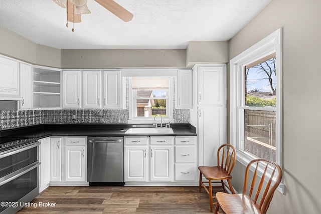 kitchen featuring open shelves, under cabinet range hood, a healthy amount of sunlight, dark countertops, and stainless steel appliances