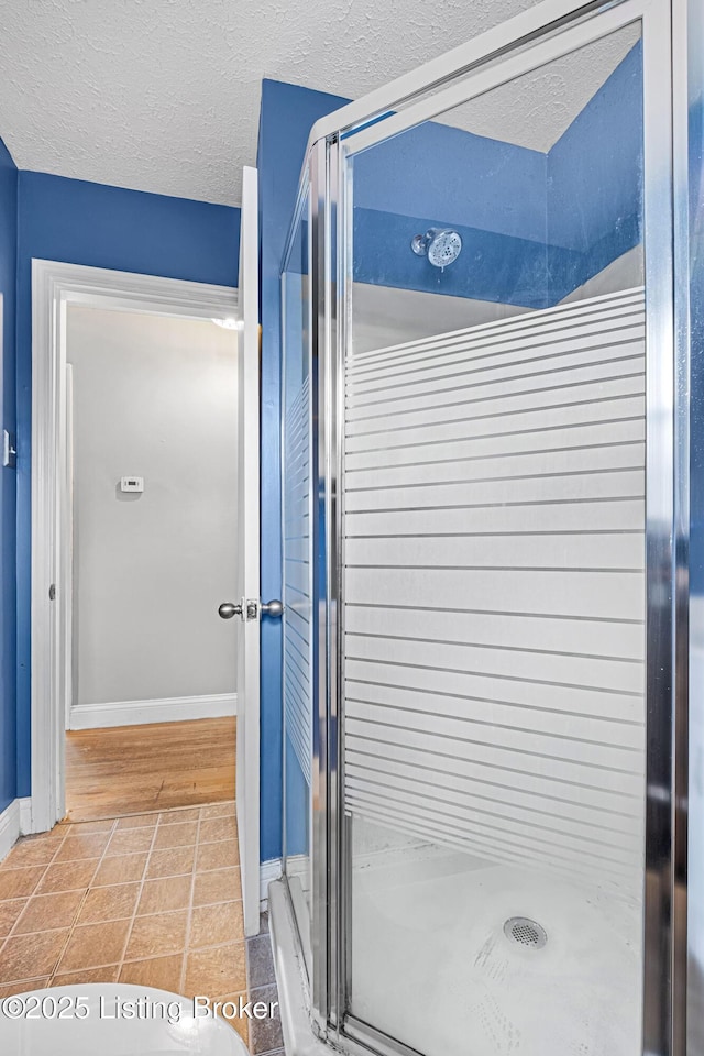full bath featuring tile patterned flooring, a textured ceiling, baseboards, and a stall shower
